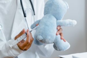 Médico aplicando vacina em ursinho de pelúcia, representando a vacinação segura de bebês na Maximune