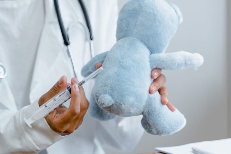Médico aplicando vacina em ursinho de pelúcia, representando a vacinação segura de bebês na Maximune